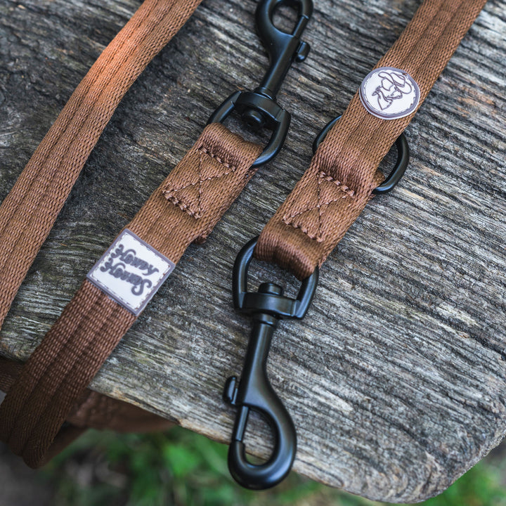 Brown dog leash with black clips and a brand logo on a wooden surface.